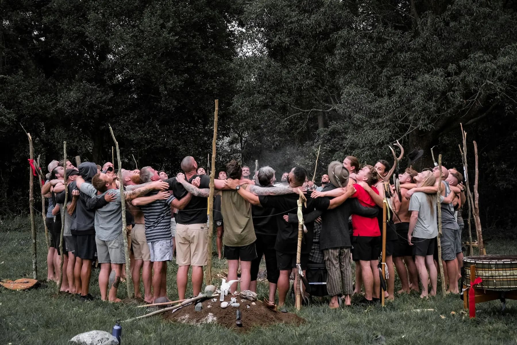 Men gathered in a closing circle around the fire at dusk, staffs planted in the earth